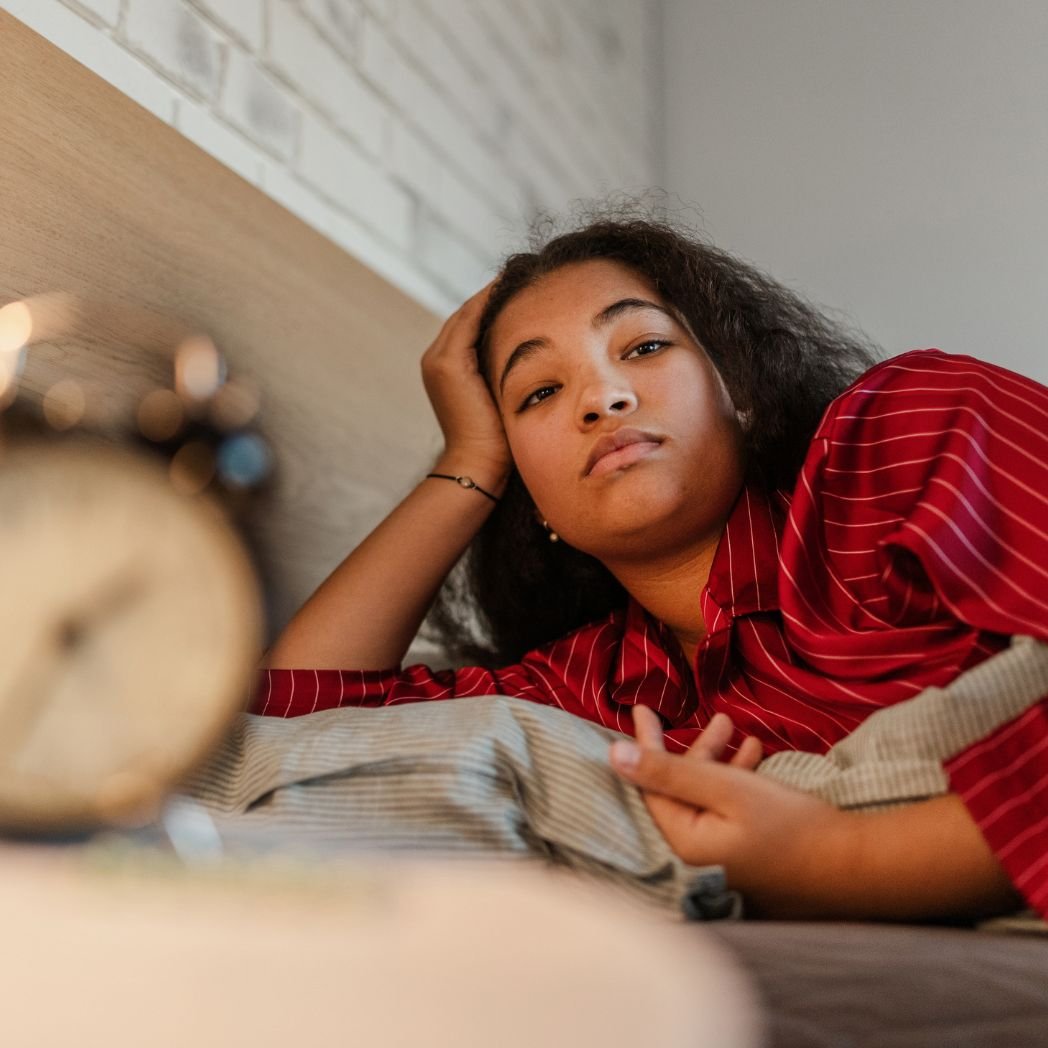 Person lying awake in bed near an alarm clock, illustrating poor sleep quality, insomnia, fatigue, and disrupted sleep associated with immune dysregulation.
