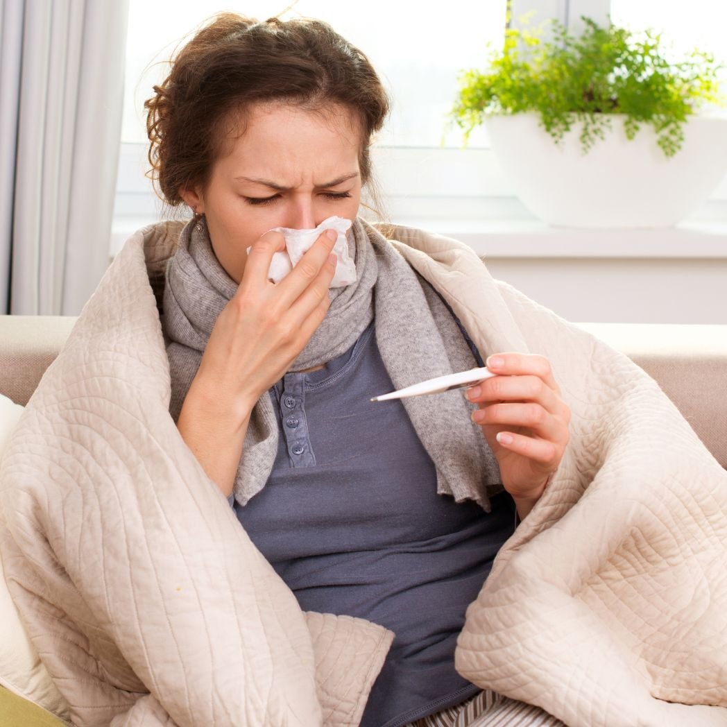 Person wrapped in a blanket checking a thermometer while dealing with cold symptoms, illustrating recurring colds, frequent infections, and immune dysregulation.